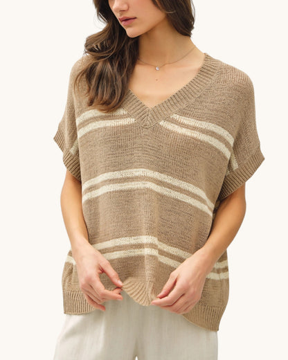 Woman wearing a taupe and white striped v-neck sweater on a white background.
