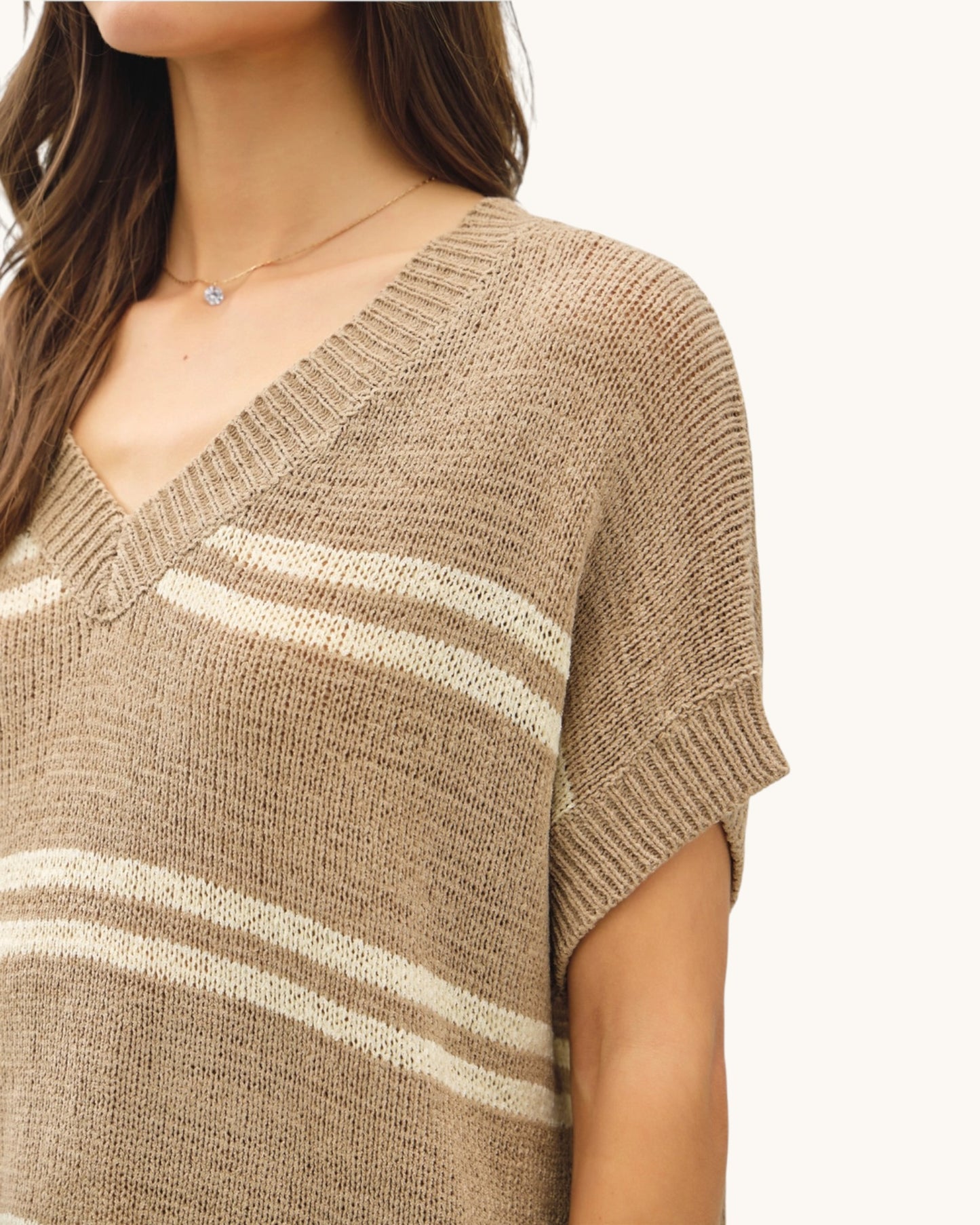 Close-up of a person wearing a taupe and white striped sweater on a plain background.