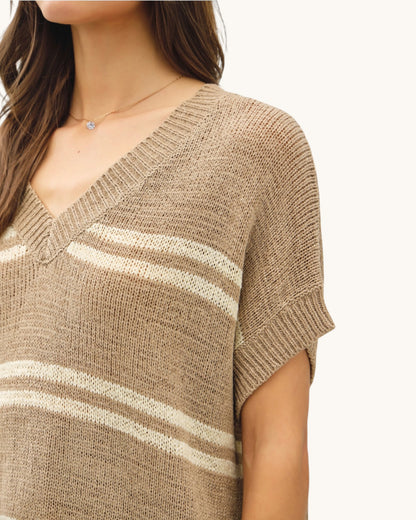 Close-up of a person wearing a taupe and white striped sweater on a plain background.