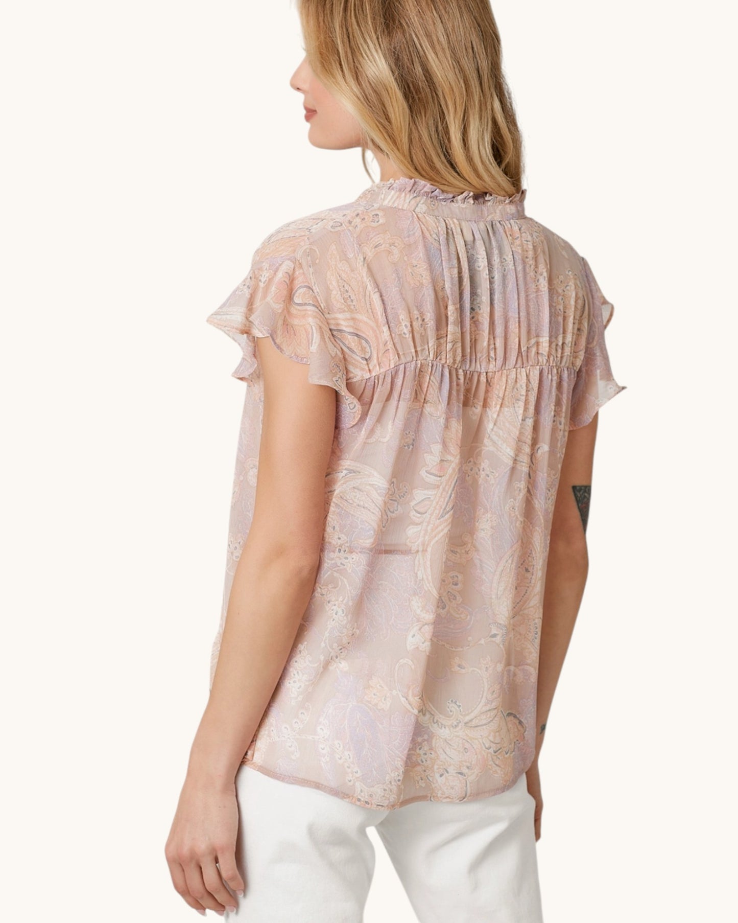 Woman wearing a sheer blush pink & paisley short sleeve button up with a white background.