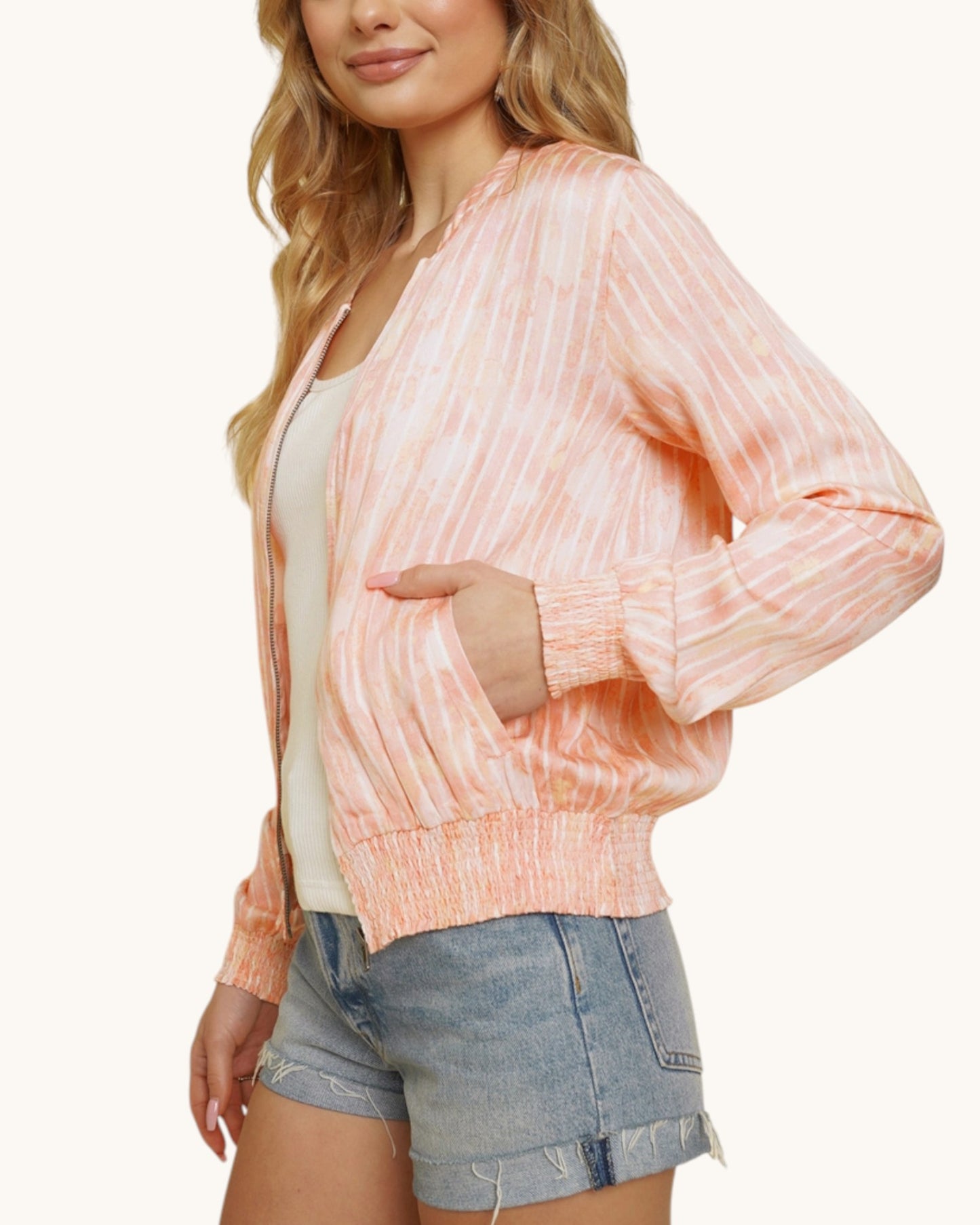 Person wearing a pinky-coral washed bomber jacket and denim shorts on a white background.