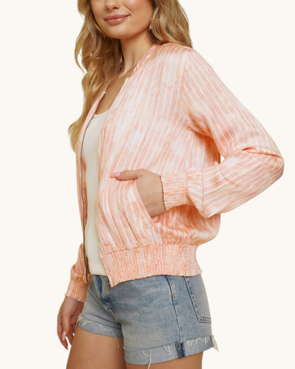 Person wearing a pinky-coral washed bomber jacket and denim shorts on a white background.