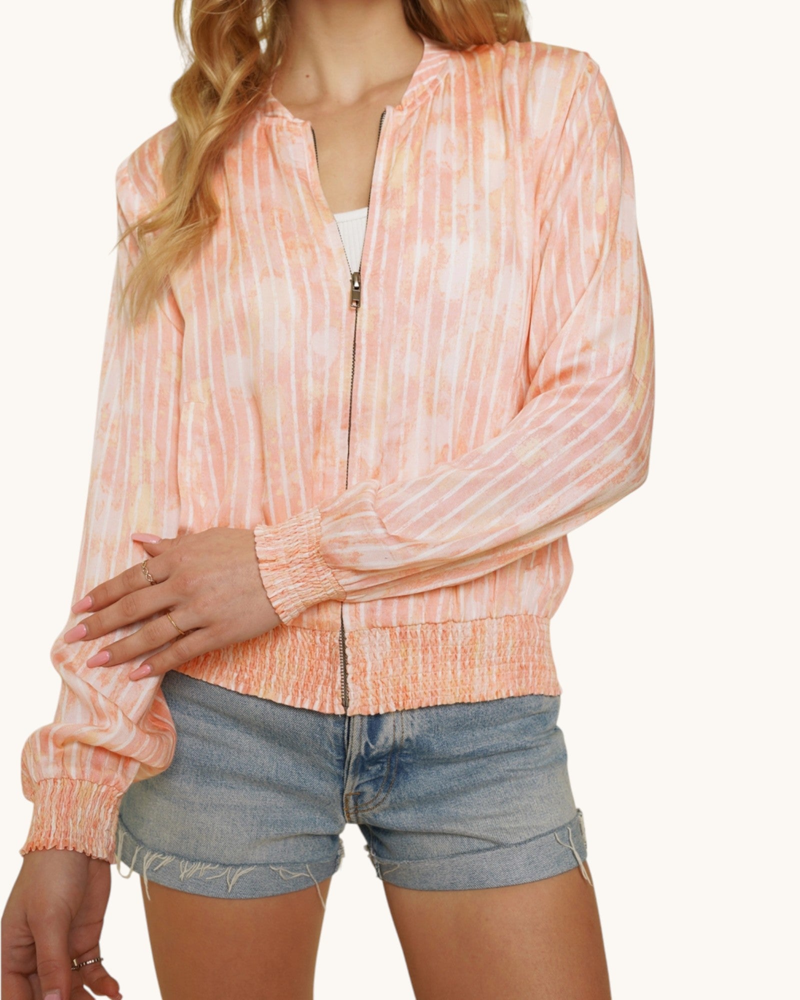 Person wearing a pinky-coral washed bomber jacket and denim shorts on a white background.