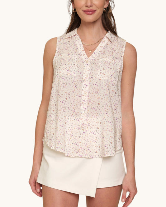 Woman wearing a sleeveless floral blouse and white shorts on a white background.