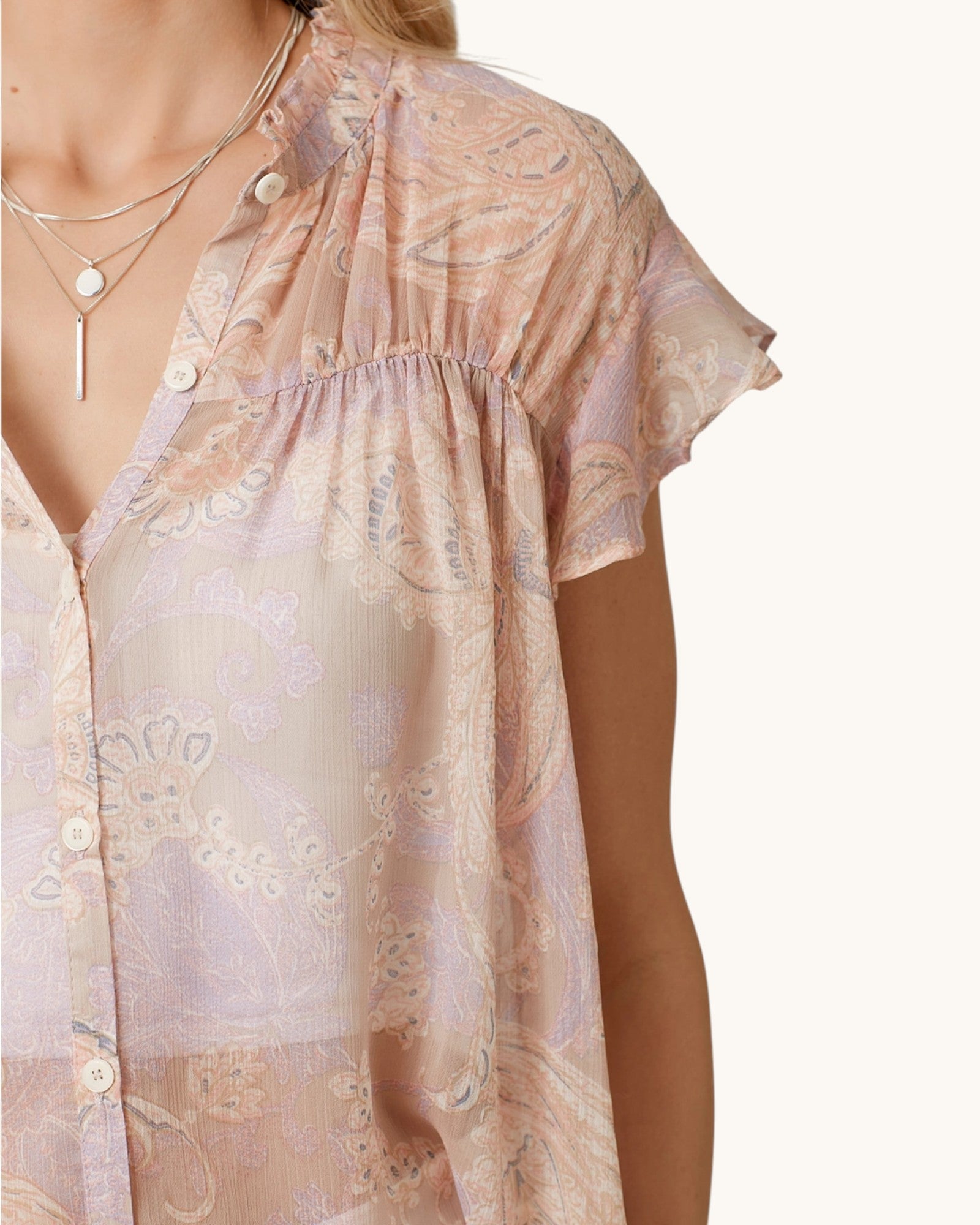 Woman wearing a sheer blush pink & paisley short sleeve button up with a white background.