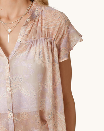 Woman wearing a sheer blush pink & paisley short sleeve button up with a white background.