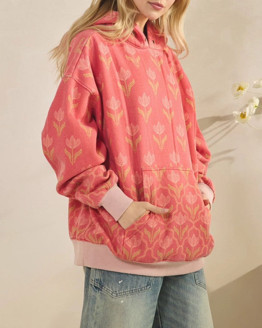 Woman wearing a pink floral/tulip hoodie against a plain background.