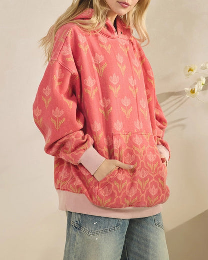 Woman wearing a pink floral/tulip hoodie against a plain background.