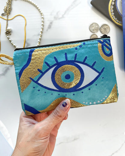 Hand holding a small turquoise zipper pouch/coin purse with an eye design against a marble background.