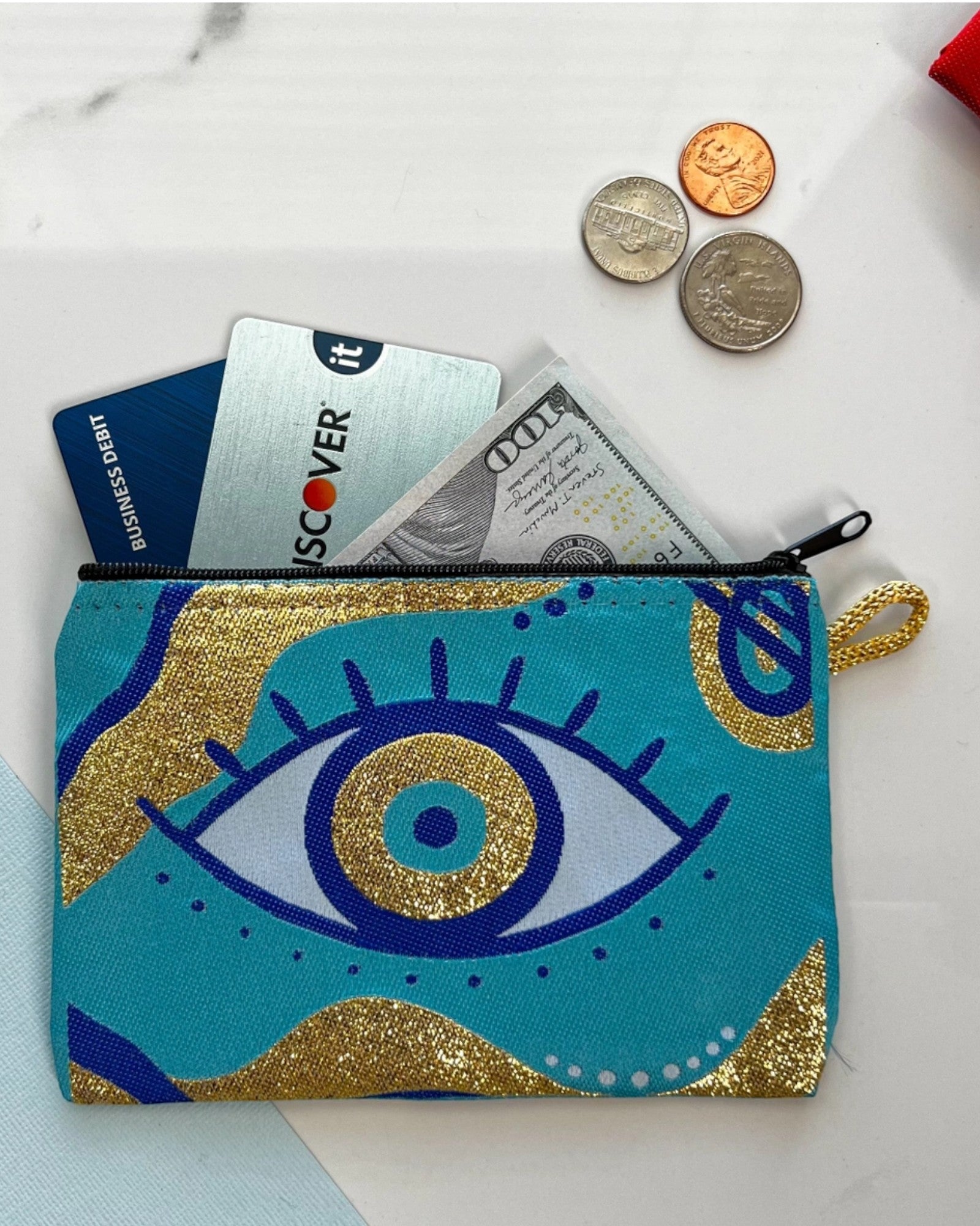 Blue pouch/coin purse with blue evil eye design containing money, cards, and coins on a marble surface.