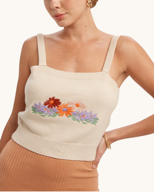 Woman wearing a beige knit tank top with floral embroidery on a white background.