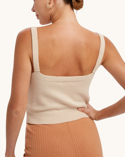 Back view of a woman wearing a beige sleeveless top with a plain background.