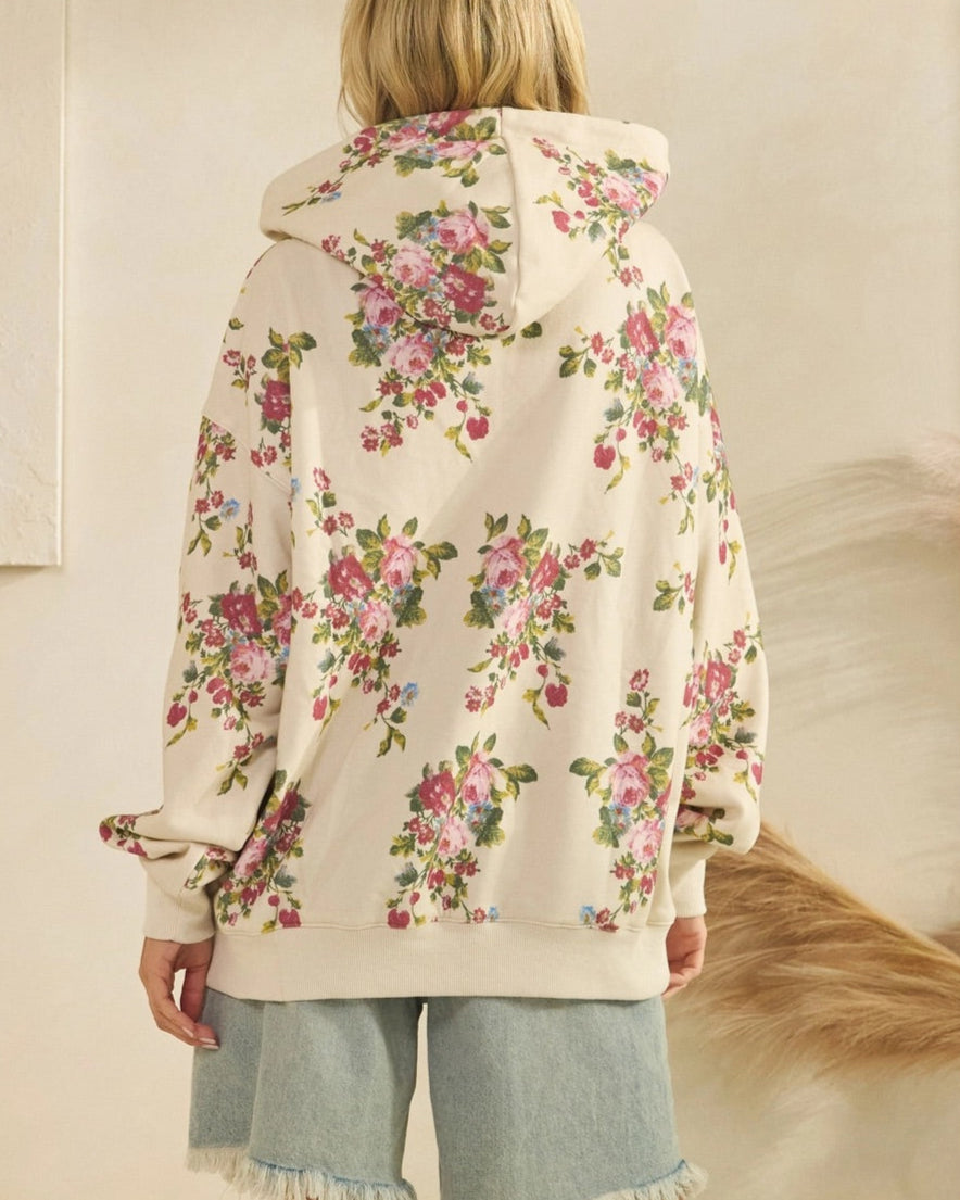 Woman wearing a floral ivory hoodie with a neutral background.