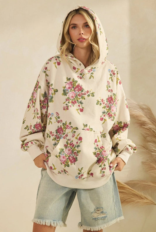 Woman wearing a floral and ivory hoodie and denim shorts against a neutral background.