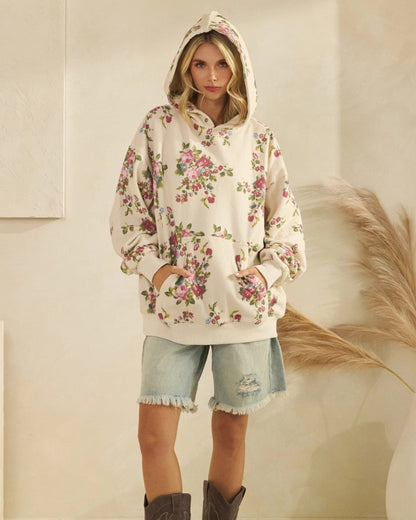 Woman wearing an ivory floral hoodie and denim shorts with brown boots in a neutral setting.