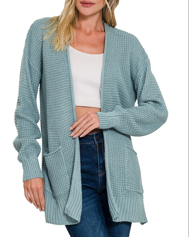 Woman wearing a blue-grey cardigan over a white top and jeans on a white background.