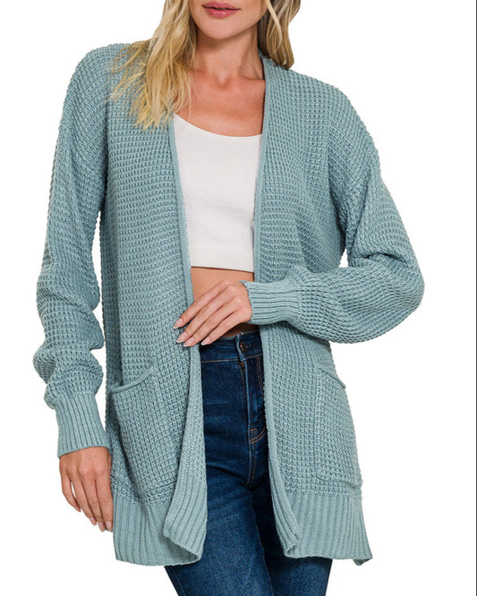 Woman wearing a blue-grey cardigan over a white top and jeans on a white background.