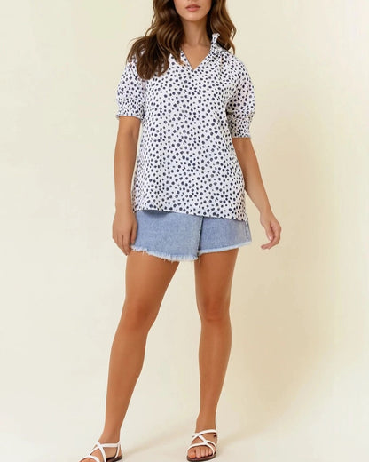 White short sleeve blouse with navy dot print and ruffled neck.