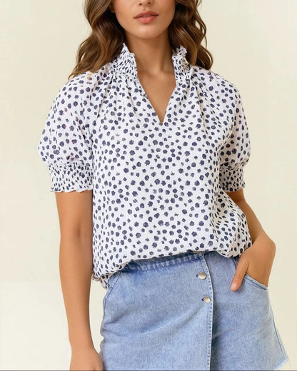 Woman wearing a white blouse with Navy polka dots and blue jeans on a beige background