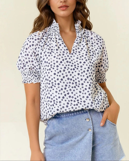 Woman wearing a white blouse with Navy polka dots and blue jeans on a beige background
