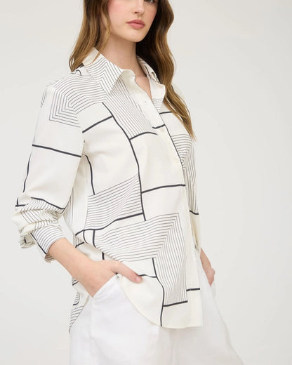 Woman wearing a white shirt with black geometric patterns on a plain background.