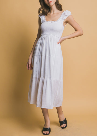 White tiered midi dress with smocked bodice, ruffle straps, and a small rosette ribbon detail at the neckline.
