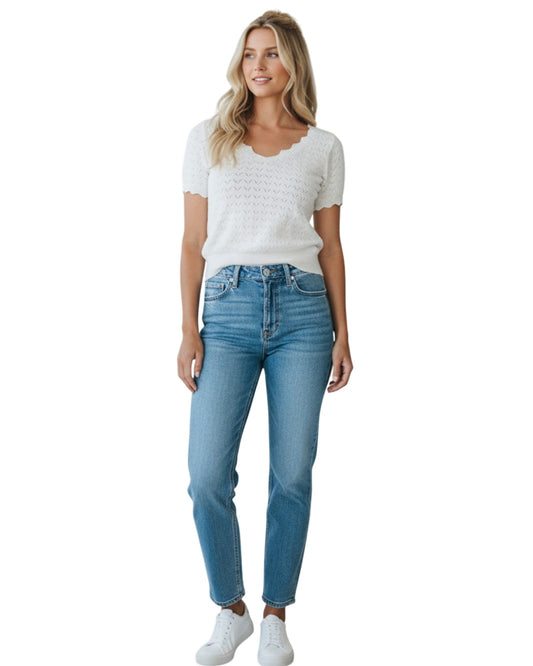 Woman wearing a white pointelle top with scallop edges and light blue jeans on a white background.