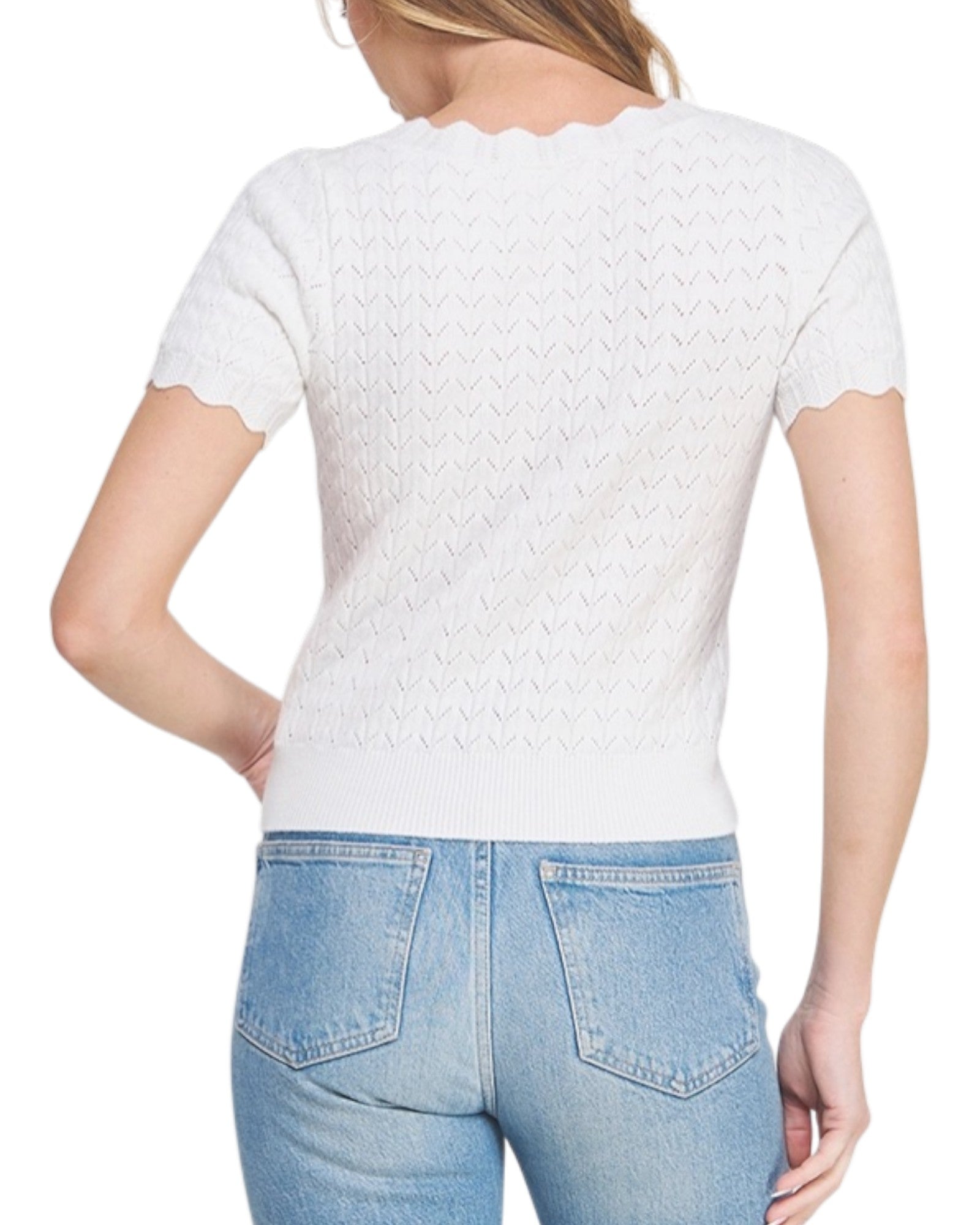Woman wearing a white pointelle top with scallop edges and light blue jeans on a white background.