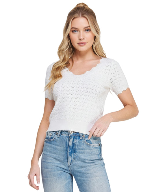 Woman wearing a white pointelle top with scallop edges and light blue jeans on a white background.