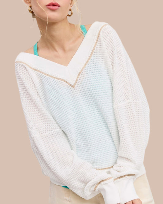 Woman wearing a white textured waffle knit long sleeve top.