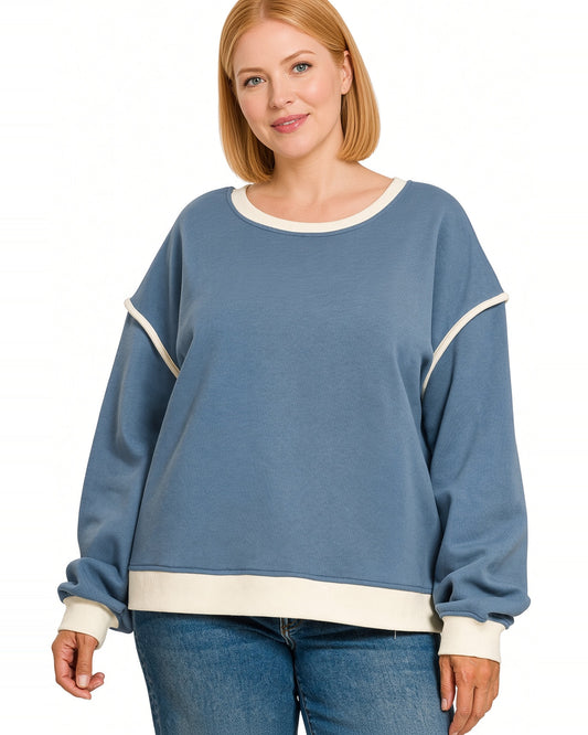 Woman wearing a blue pullover sweatshirt with a round neckline and contrast ivory trim on hem, neckline and cuffs.