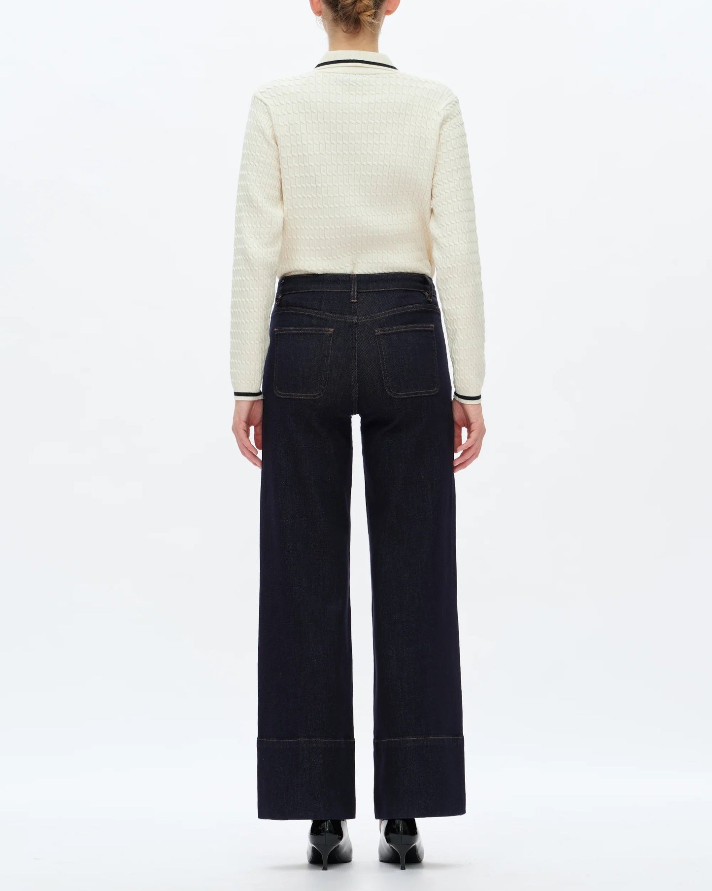 Person wearing a white sweater and dark pants on a white background.