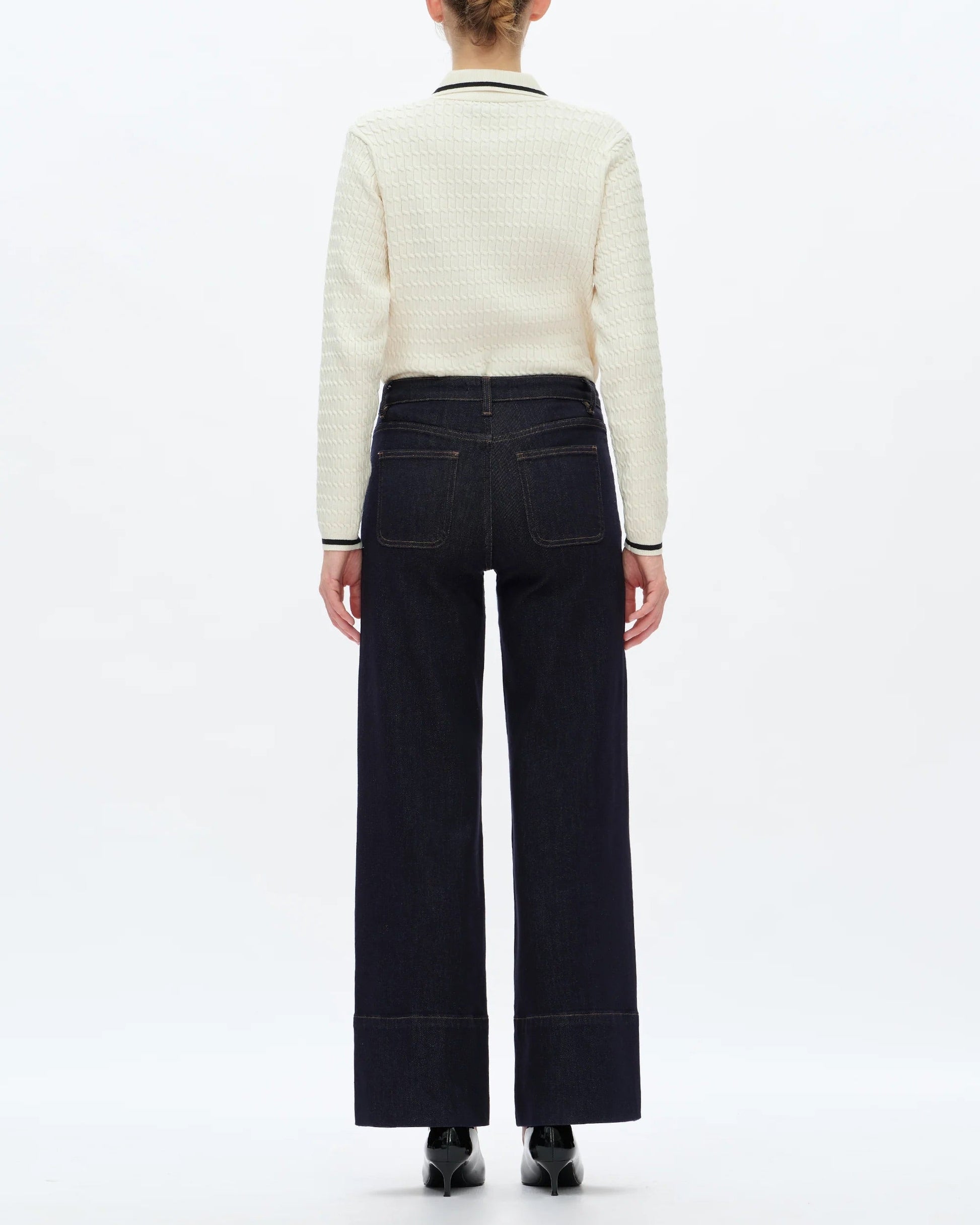 Person wearing a white sweater and dark pants on a white background.