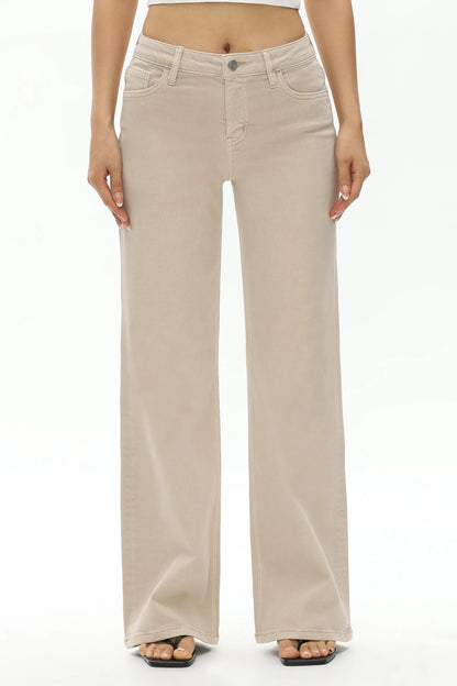 A model from the waist down wearing a pair of light beige wide-leg jeans, paired with black flat sandals, against a plain white studio background.