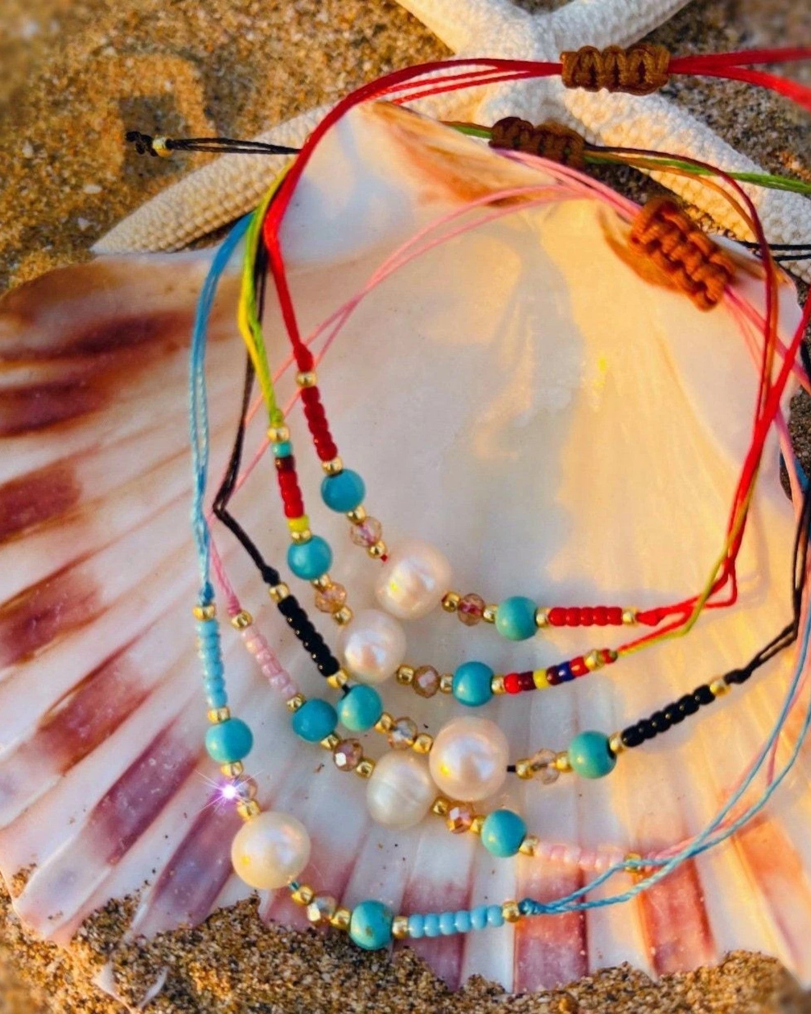 Colorful beaded bracelets on a seashell with sand background.