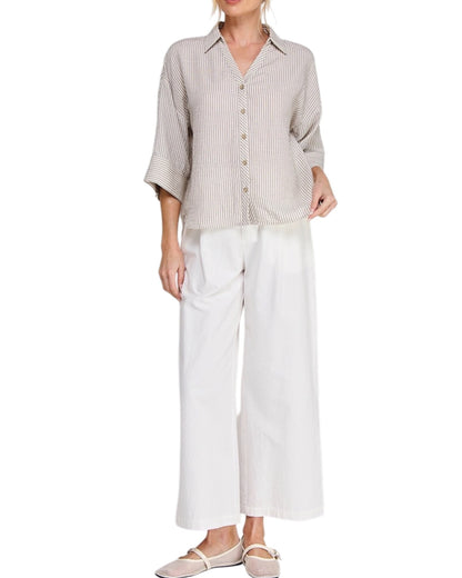 Woman wearing a beige striped shirt and white pants on a white background.