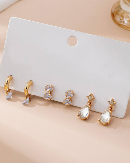 Set of gold and crystal earrings on a white card with a beige background.
