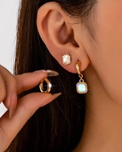 Woman wearing two crystal and gold earrings and holding a small hoop crystal and gold huggie earring. 