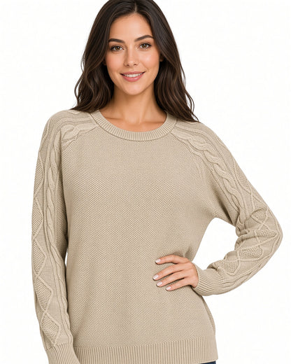 A woman wearing a beige cable-knit crewneck sweater, posing against a solid white background.