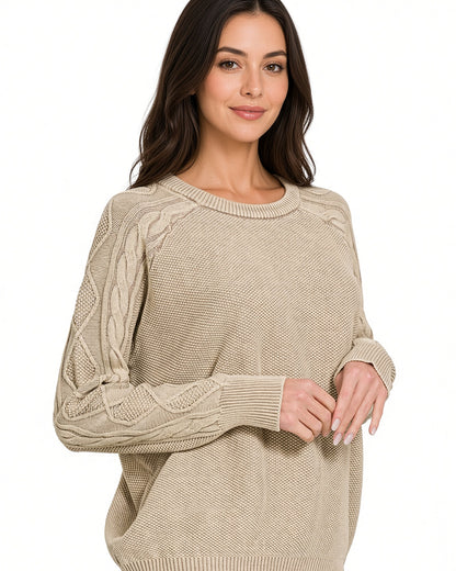 A woman wearing a beige stonewashed cable-knit crewneck sweater, shown from the waist up against a plain white background.