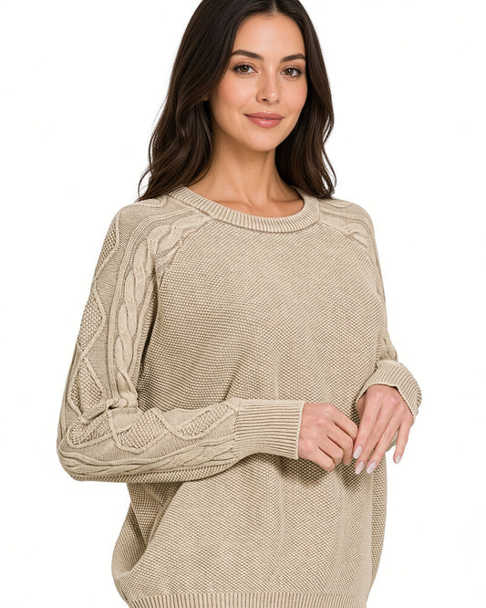 A woman wearing a beige stonewashed cable-knit crewneck sweater, shown from the waist up against a plain white background.