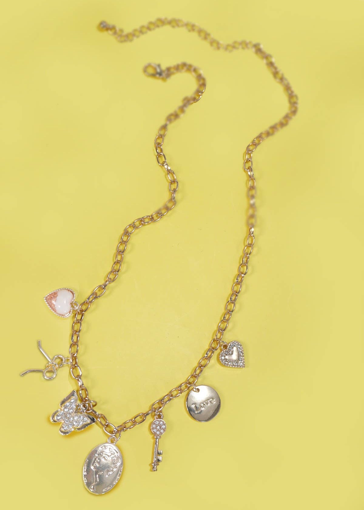 Gold charm necklace with a bow, wishbone, heart, key, butterfly, and sparkling rhinestone accents.