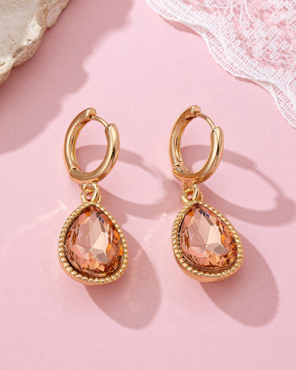 Gold hoop earrings with teardrop-shaped peach gemstones on a pink background.
