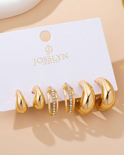Set of gold hair earrings on a branded card against a beige background.