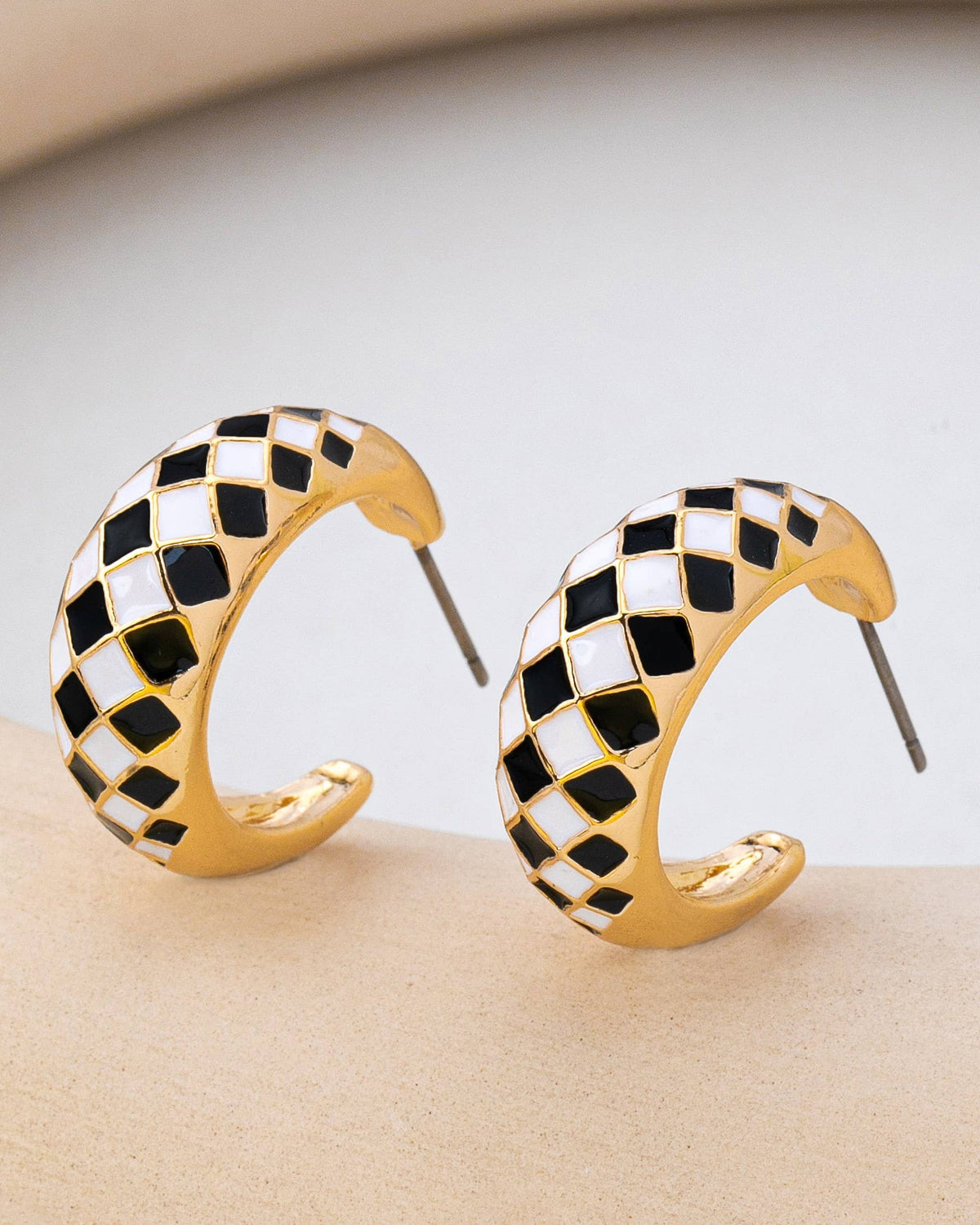 Gold hoop earrings with black and white checkered pattern on a beige surface.