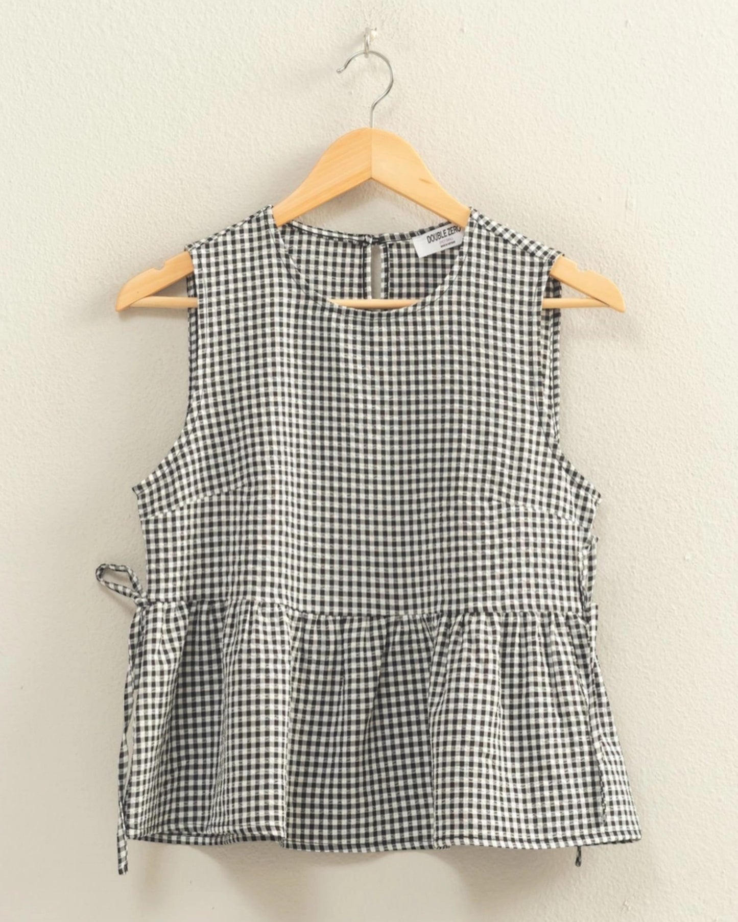 Black and white checkered sleeveless top on a hanger against a beige background