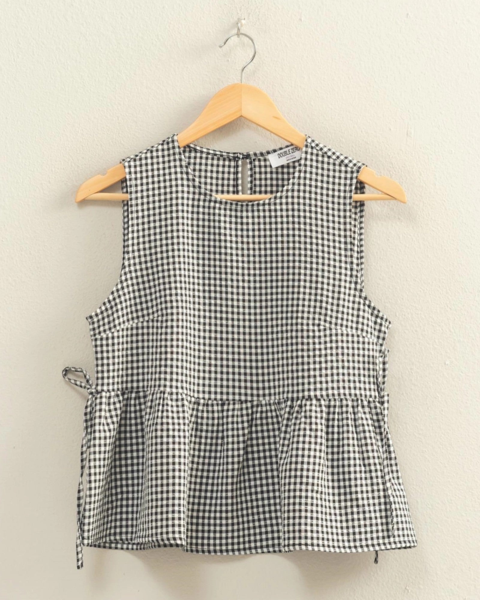 Black and white checkered sleeveless top on a hanger against a beige background
