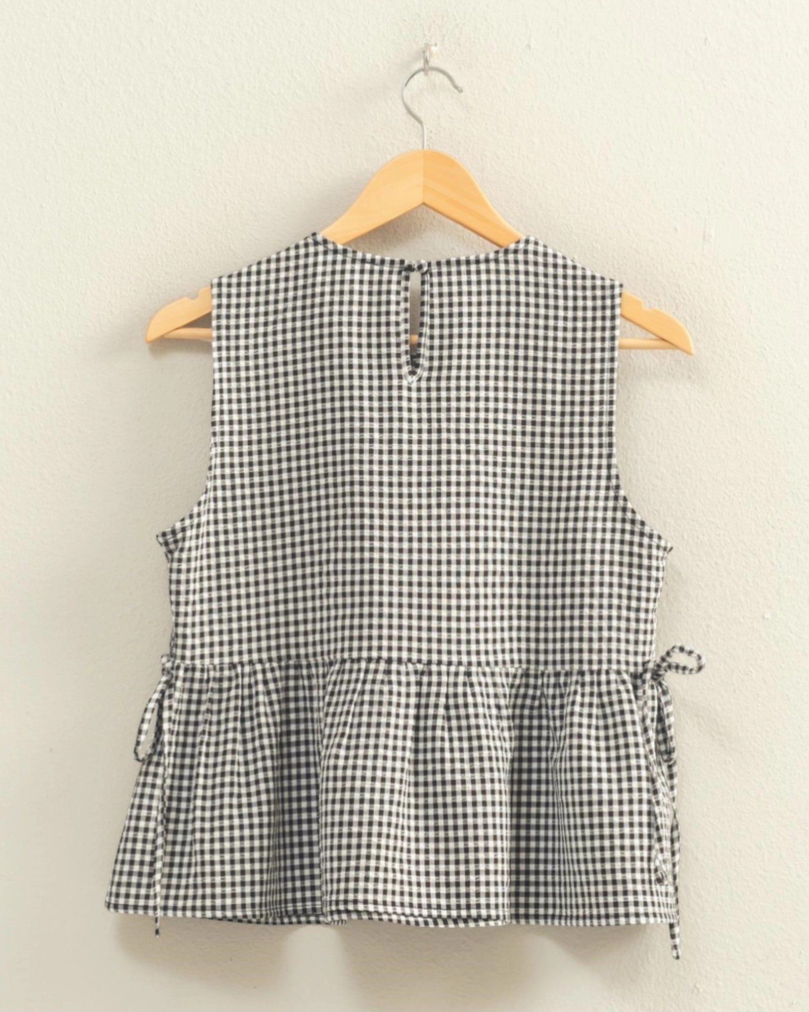 Black and white checkered sleeveless top on a hanger against a beige background.