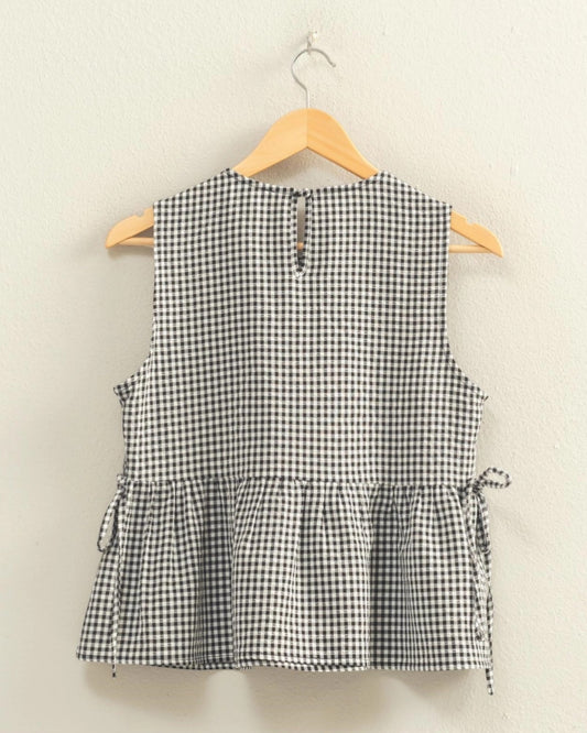 Black and white checkered sleeveless top on a hanger against a beige background.