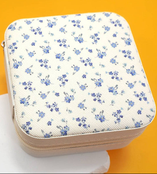 An off-white zippered case with a blue floral pattern, displayed on a white surface against a bright orange background. 